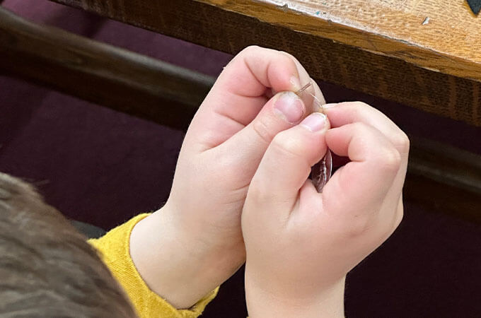 Child threading a needle with a wire needle threader