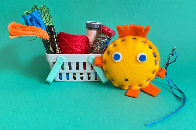 hand sewn felt toy holding a pin and chenille needle